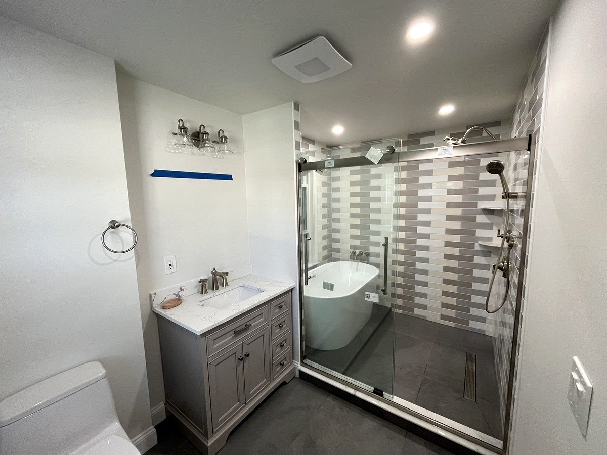 Bathroom remodel Watertown MA - gray vanity with white countertop, three-globe light bar, and glass shower enclosure