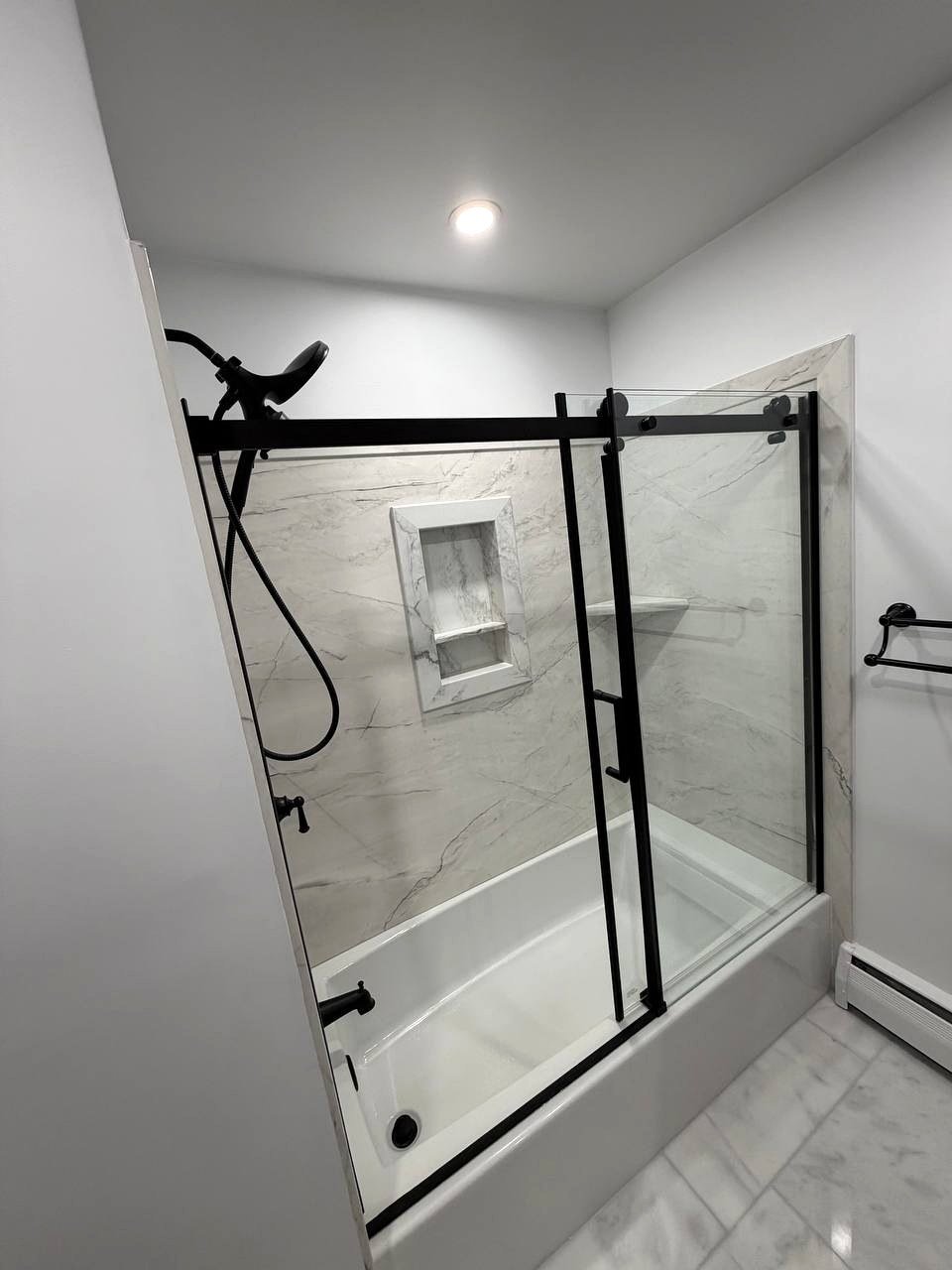 Bathroom renovation Norwood MA - bathtub with black sliding glass door and marble panels