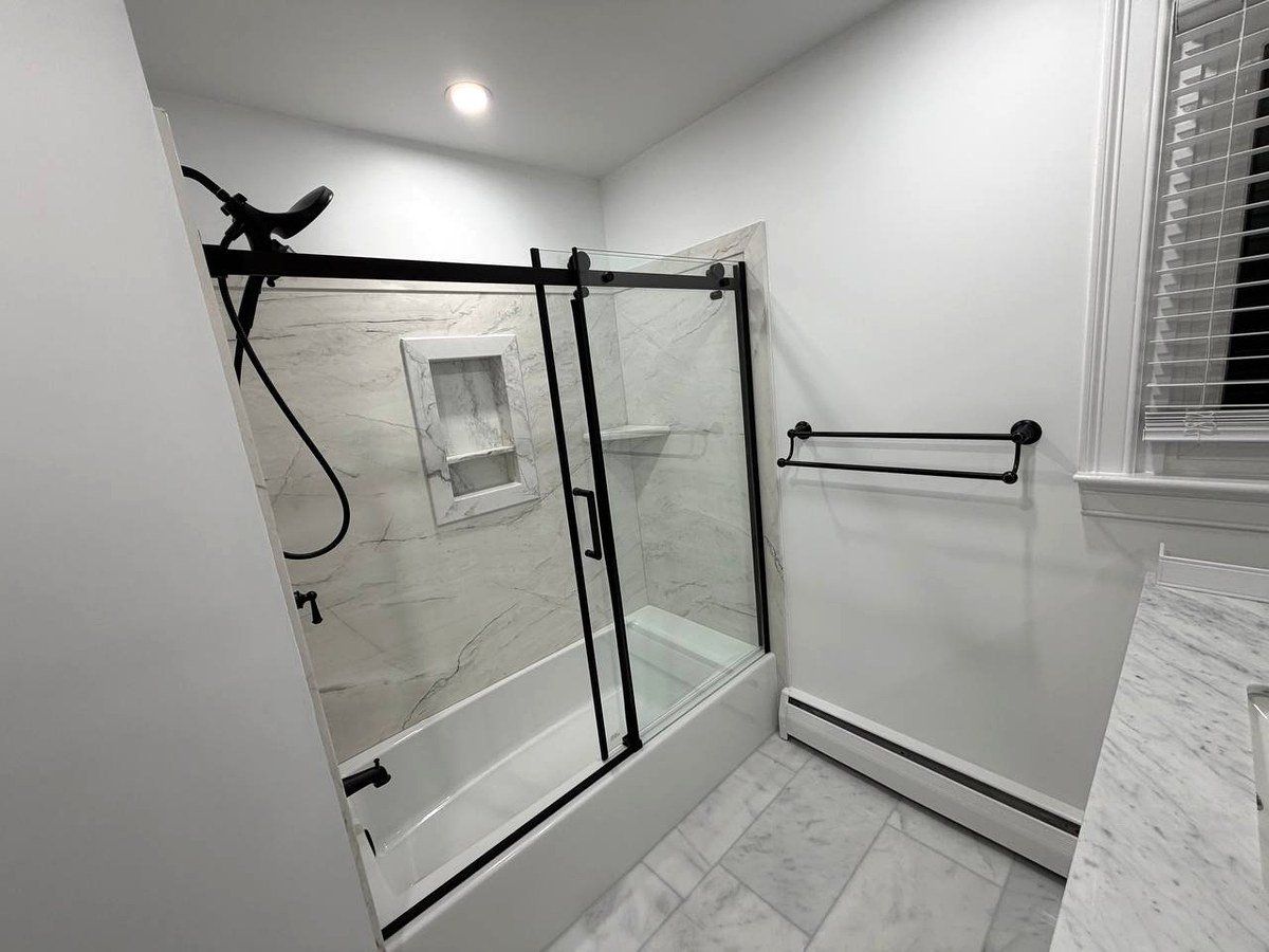 Completed bathroom renovation Norwood MA - full room view with bathtub glass door and marble tiles