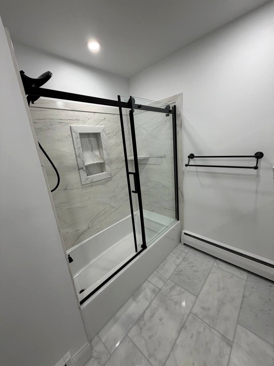 Bathroom renovation Norwood MA - marble floor tiles and baseboard heater with black towel bar