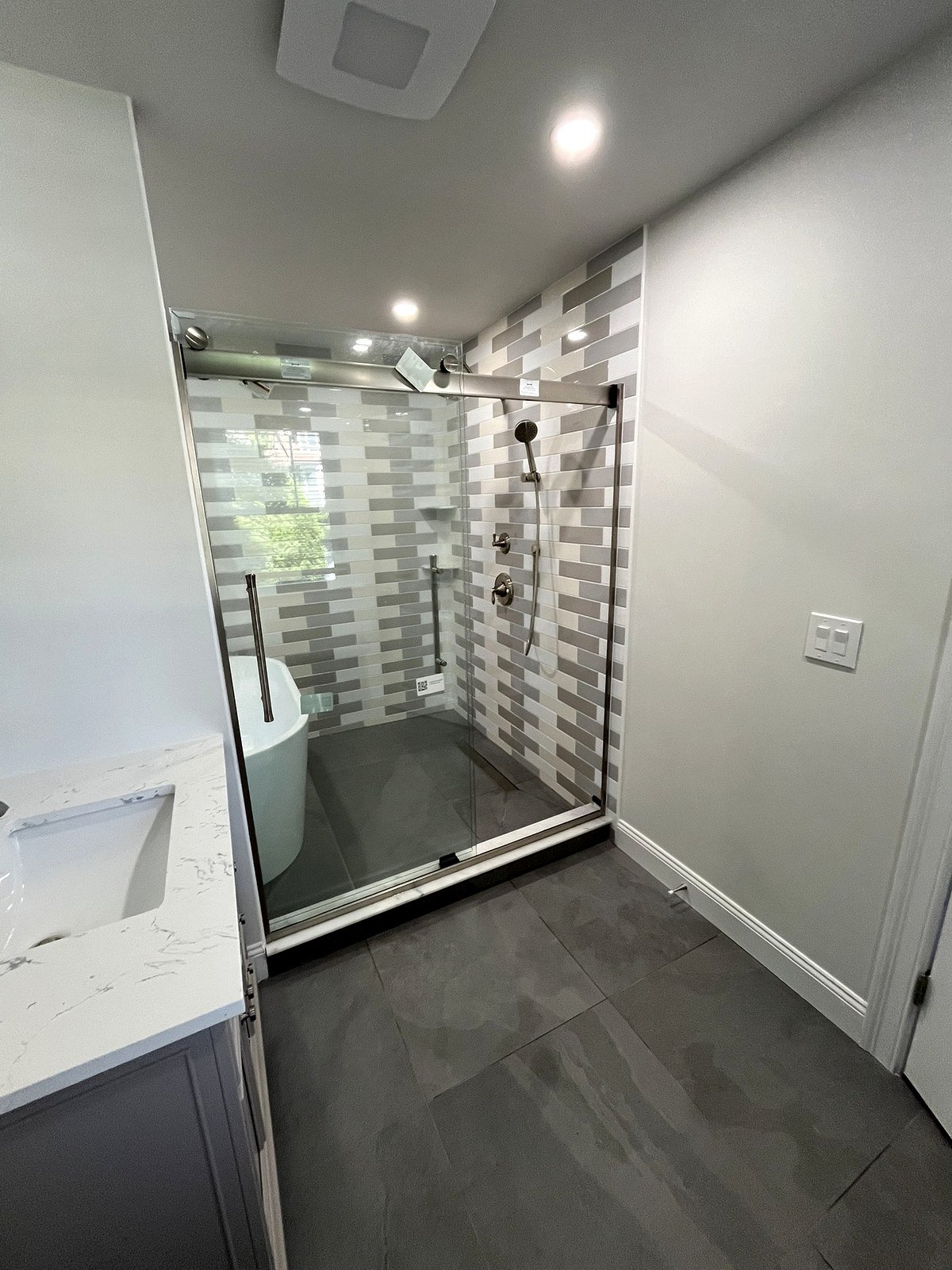Bathroom renovation Watertown MA - walk-in shower with sliding glass door, freestanding soaking tub, and horizontal gray tile