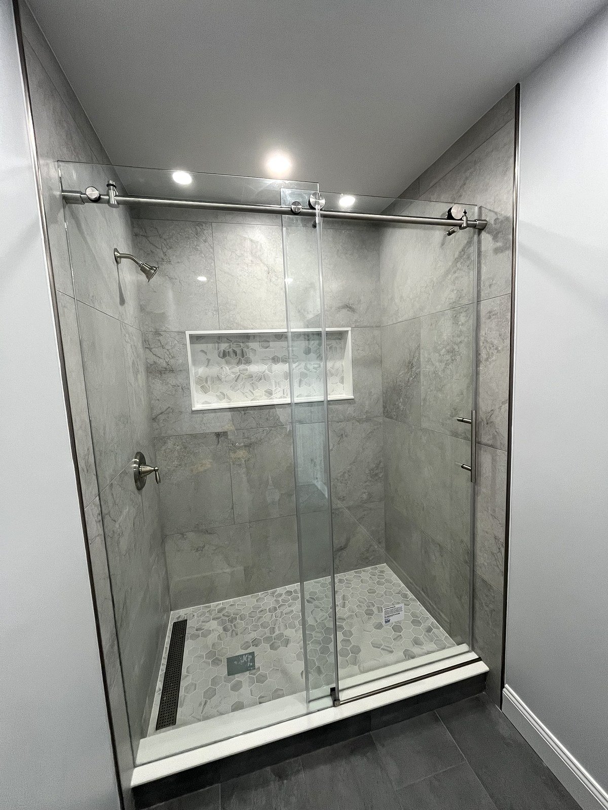 Walk-in shower renovation Newton MA - sliding frameless glass door with gray marble-look tile and hex mosaic floor