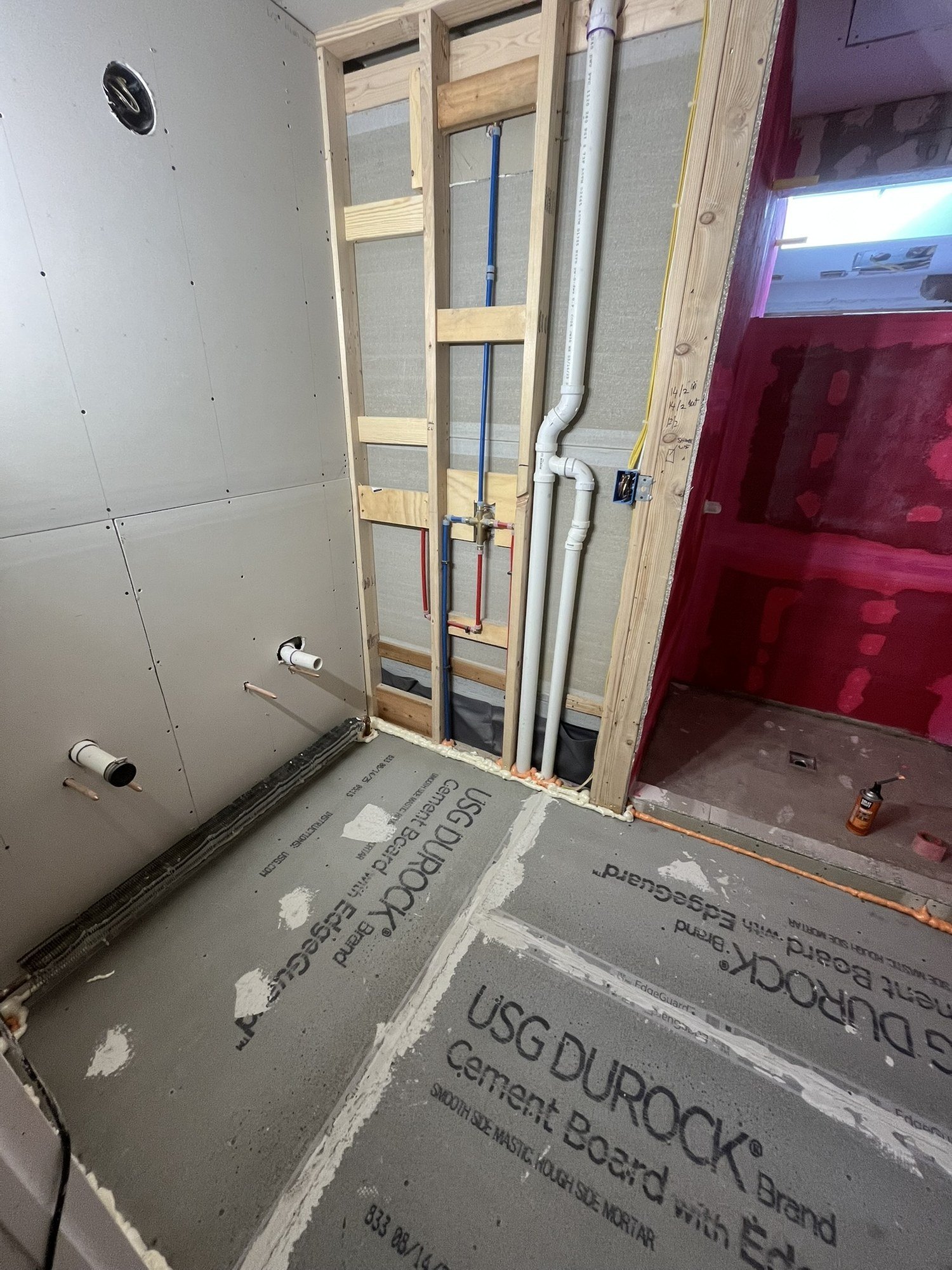 Cement board floor and walls with the shower area coated in red waterproofing membrane