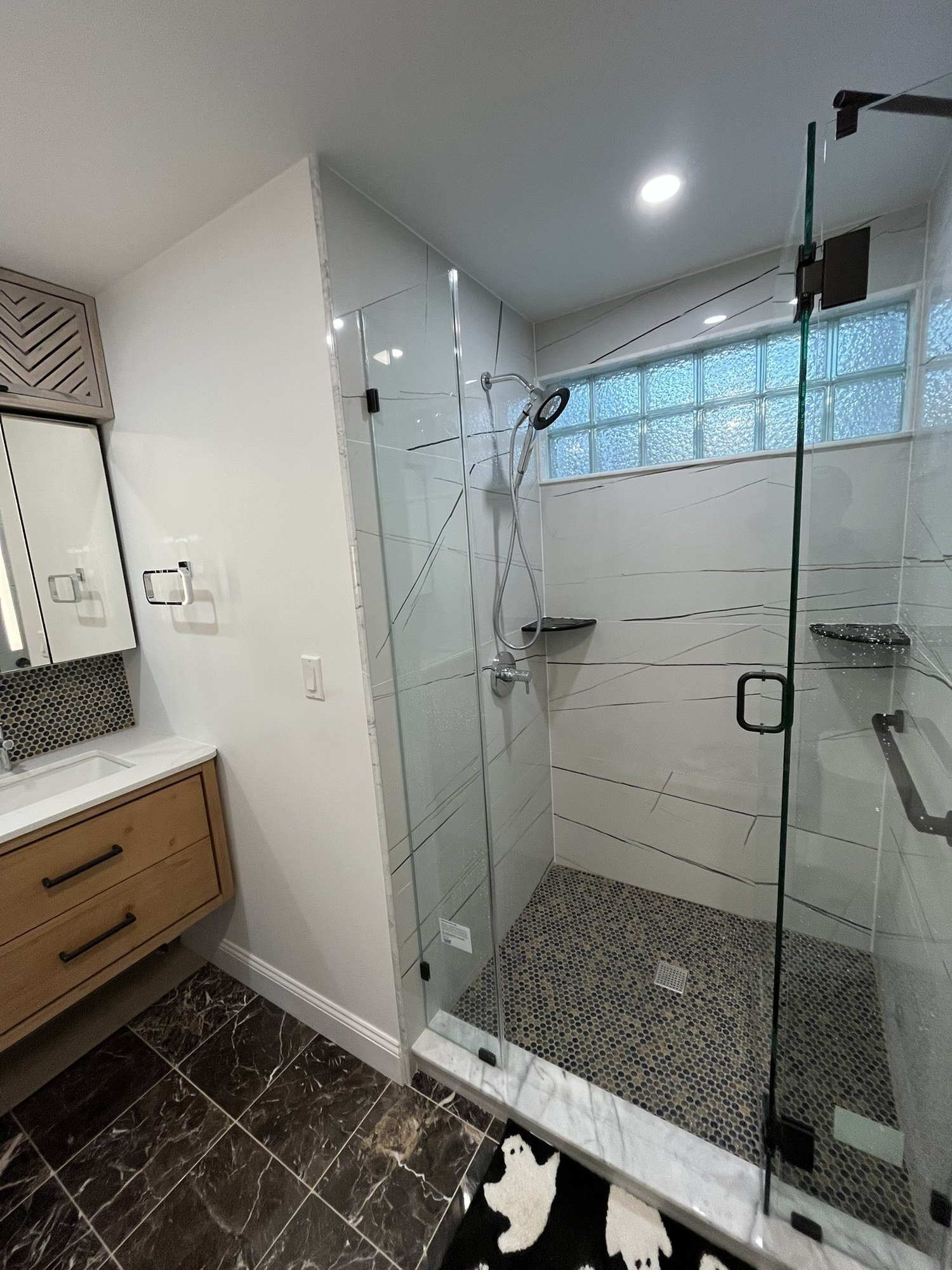 Finished walk-in shower with frameless glass, pebble tile floor and glass-block window